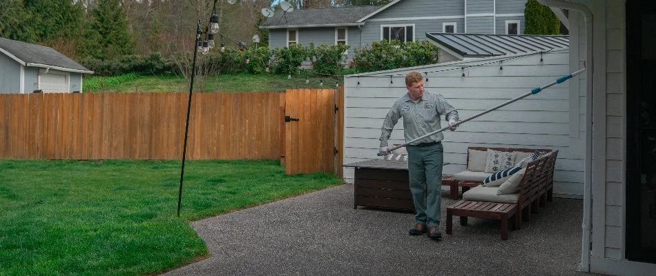 Worker in a backyard in Bremerton, WA, sweeping a house for spiders.