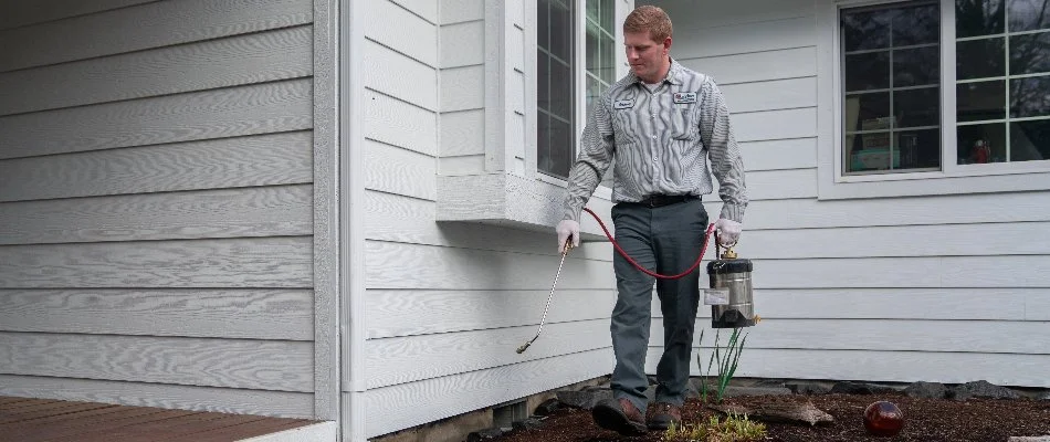 Worker spraying pest treatment on side of home in Bremerton, WA.